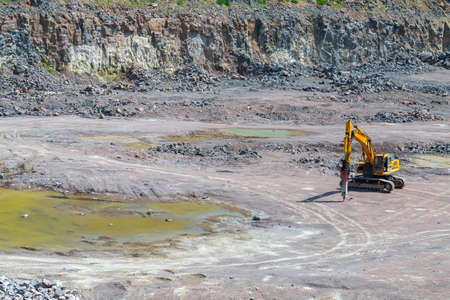 A large tracked excavator attachment of pneumatic hammer in a quarry open pit mining of granite...