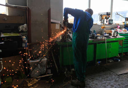 Male mechanic working tool Angle grinder in the garage for car repairs. Sparks fly out of under the...