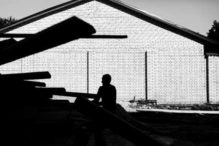 A worker unloads on the construction of wooden boards on a background of a brick wall. Black and white photo of high contrast. Unrecognized face of person.の写真素材
