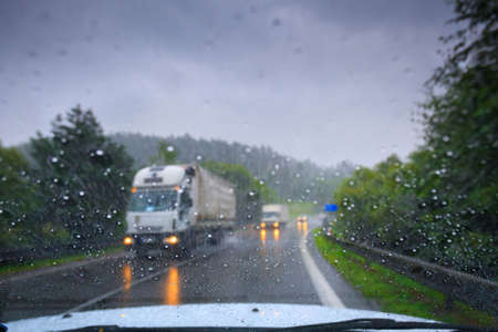 Through the car's windshield view on the highway and oncoming traffic in a storm. Drops of water on the glass. Image in the art defocus.の写真素材