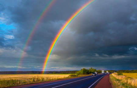 After an evening summer showers. A bright rainbow stands over the highway. Trucks and passenger cars go on the wet asphalt. Real photo - montage or graphic software was not used.の写真素材