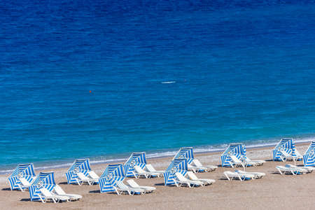 Colorful umbrellas and sunbeds on an empty beach resort - vacation concept on Greece islands in Aegean and Mediterranean seasの写真素材