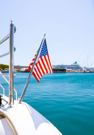 The flag of the United States flutters in the wind on a stainless steel flagpole at the stern of a motor yacht. Marina in the port city in beautiful summer sunny weather.の写真素材