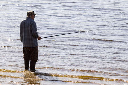 Fishing as a hobby. A man fishing with a fishing rod on the shore of a pond, river or lake, will spend his free time.の写真素材