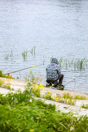 Fishing as a hobby. A man fishing with a fishing rod on the shore of a pond, river or lake, will spend his free time.の写真素材