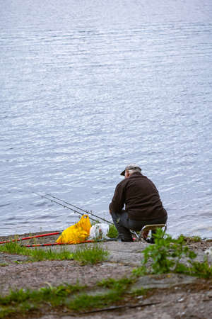 Fishing as a hobby. A man fishing with a fishing rod on the shore of a pond, river or lake, will spend his free time.の写真素材