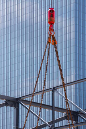 Crane hoisting block with hook on steel chain on steel rope. Glass facade of a modern skyscraper in the background. Loading\unloading of building materials on construction building site. Development.の写真素材