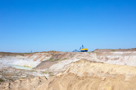 Quarry extraction porcelain clay(kaolin) and quartz sand in the open pit mine. Powerful industrial walking excavator on the site.の写真素材