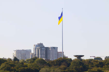 Bright evening cityscape of the big city on the hill over wide river Dnipro in awesome bright sunset in Kyiv, Ukraine. View at largest ukrainian national flag on flagpole.の写真素材