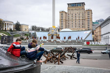 KYIV, UKRAINE - APR 20, 2022: Anti-tank hedgehogs or Czech hedgehogs on the side of the road are ready to block Independence Square in the event of an attack. Children have fun near the monument.のeditorial素材