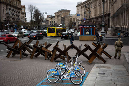KYIV, UKRAINE - APR 20, 2022: Anti-tank hedgehogs or Czech hedgehogs on the side of the road are ready to block Independence Square in the event of an attack. Sharing company bikes in the foreground.のeditorial素材