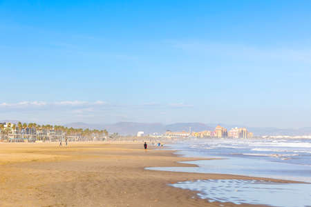 Summer vibes on the sunny autumn beach of Malvarrosa in Valencia, Spain. Vast expanses of smooth fine sand on the sea coast attract vacationers to solitary walks along the bubbling foamy waves.の写真素材