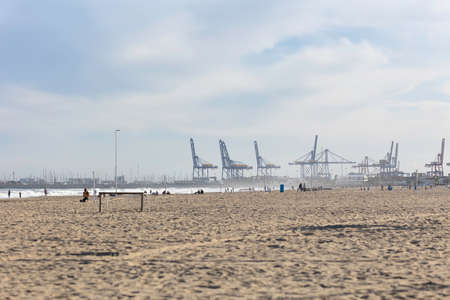 Summer vibes on the sunny autumn beach of Malvarrosa in Valencia, Spain. Vast expanses of smooth fine sand on the sea coast attract vacationers to solitary walks along the bubbling foamy waves.の写真素材