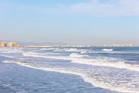 Summer vibes on the sunny autumn beach of Malvarrosa in Valencia, Spain. Vast expanses of smooth fine sand on the sea coast attract vacationers to solitary walks along the bubbling foamy waves.の写真素材