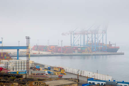 Odesa, Ukraine - OCT 22 2019: Autumn fog in the sea cargo port with side loaders. Gantry cranes and...
