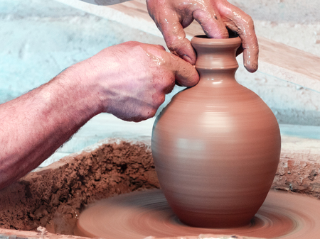 Hands of a Potter making a vase with a narrow neck on the pottery wheel.