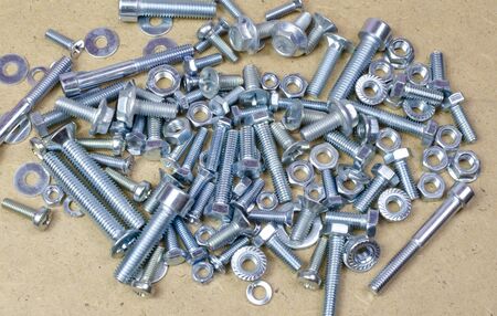 Collection of new bolts, screws, nuts of engineering metal tools on a wooden table backgroundの写真素材