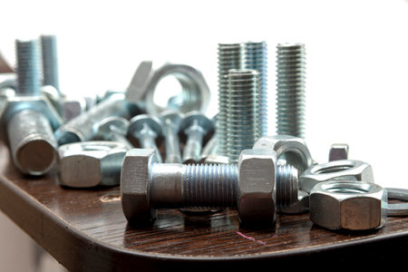 Several metal bolts and nuts on a wooden table next to a white backgroundの写真素材