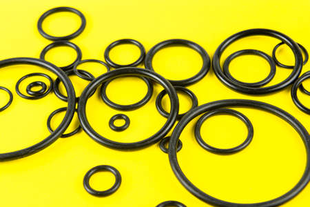 Black hydraulic and pneumatic O-rings in different sizes on a yellow background. Sealing gaskets for...