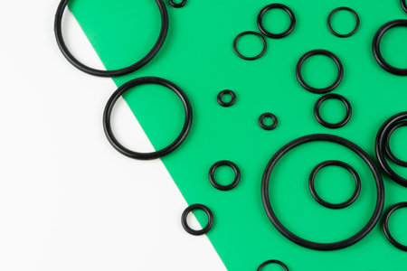 Black hydraulic and pneumatic O-rings in different sizes on a green and white background. Rubber rings. Sealing gaskets for hydraulic connections. Rubber sealing rings for plumbing. View from aboveの写真素材