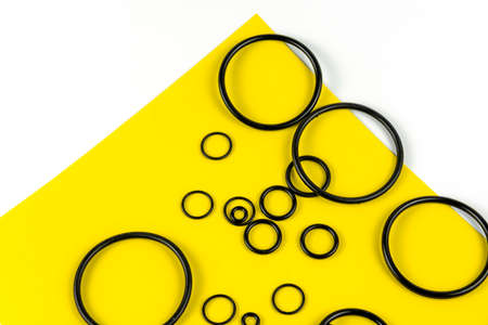 Black hydraulic and pneumatic o-rings in different sizes on a yellow and white background. Rubber rings. Sealing gaskets for hydraulic connections. Rubber sealing rings for plumbing. View from aboveの写真素材