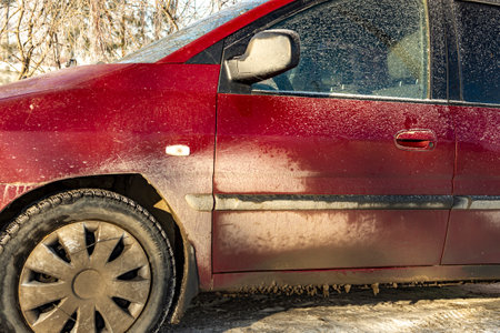 Dirty red car in the winter early morning, dirt stuck after driving on a winter city road. Concept...