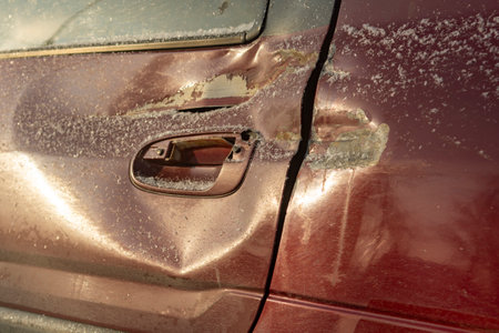 Red car door dented after accident, car hit. Impact damage. Damaged rear door of car, dent after road collision. cool winter morningの写真素材