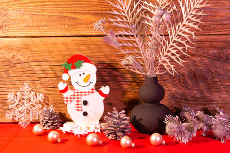Christmas decoration, the figure of a snowman on a red table against the background of an old wood wall, silver bubbles for the Christmas tree, silver plants in a black vase.の写真素材