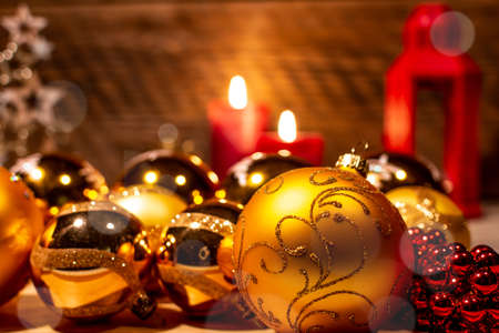 Christmas decoration. Lantern, golden Christmas tree and red bubbles, lit candles, cones on the background of a wall of old damaged wood.の写真素材