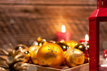 Christmas decoration. Lantern, golden Christmas tree and red bubbles, lit candles, cones on the background of a wall of old damaged wood.の写真素材