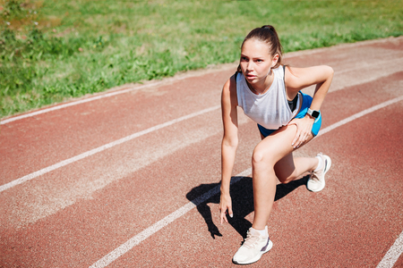Young athletic girl athlete preparing to run at the stadium, outdoors. The concept of a healthy...