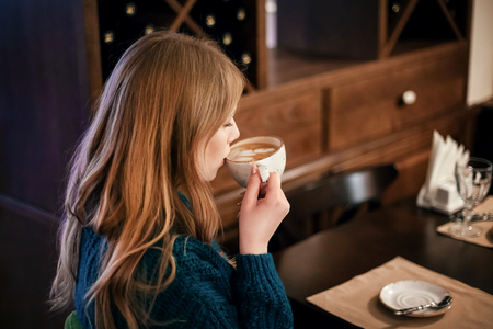 beautiful young woman in a cozy cafe drinking cup coffeeの写真素材