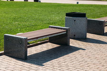 Wooden and stone park bench and a garbage bin for waste in a city park