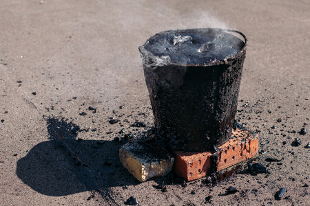 Molten hot tar in a bucket on the bricks. Roof repair. Smoke from the bucketの写真素材