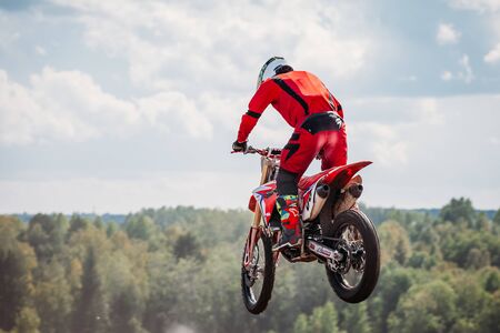 Lebedyanka, Russia - August 25, 2019: Russian Motocross Championship, motorbike and motorcycle races off-road cross-country. athlete jumps in flight on springboard against blue sky.のeditorial素材