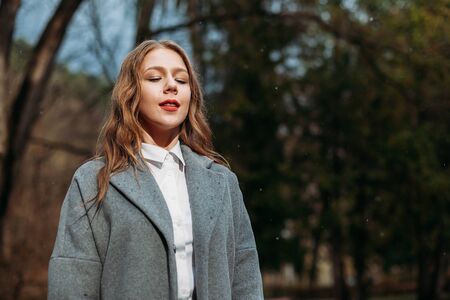 Portrait of a young girl businesswoman in a grey coat posing in Park in autumnの写真素材