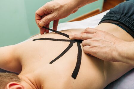 physical therapist placing kinesio tape on patient s backの写真素材