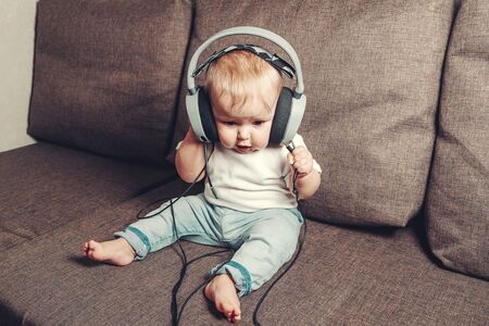 The child learns the world. A little happy child is sitting on the bed in big headphones and...