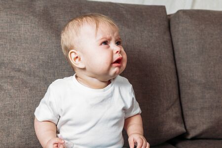 little cute baby boy or girl is capricious and starting crying close up portrait inside