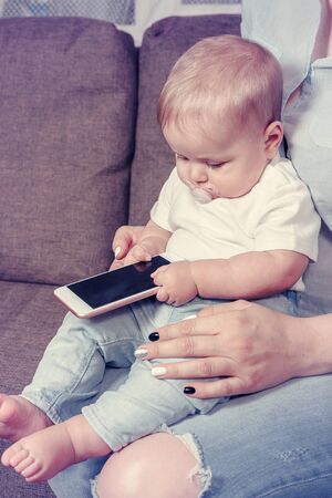 mother showing smart phone content to his baby son sitting on a couch in the living room at home