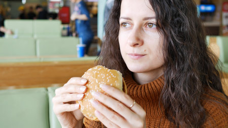 Young beautiful smiling woman eating a burger in cafe.の写真素材