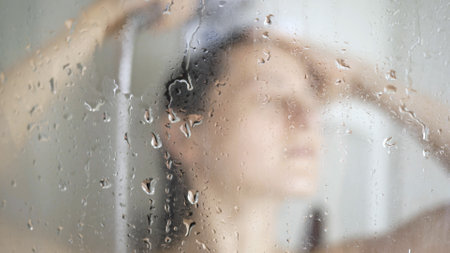 Beautiful girl taking shower behind glass, selective focus on glass drops water.の写真素材