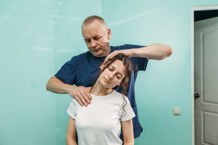 physiotherapist is rehabilitating young woman neck in medical officeの写真素材