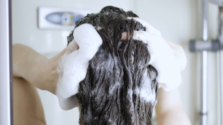 Young woman washes hair with shampoo in shower. Hair care, rinse shampoo.の写真素材