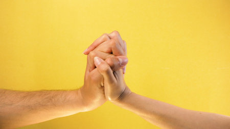 Male and female hand together. Male hand hugs female hand isolated on yellow background.