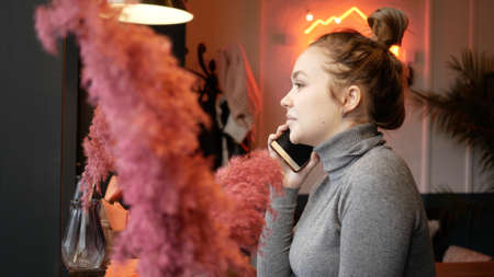 Beautiful young woman in cafe talking on phone at window.の写真素材
