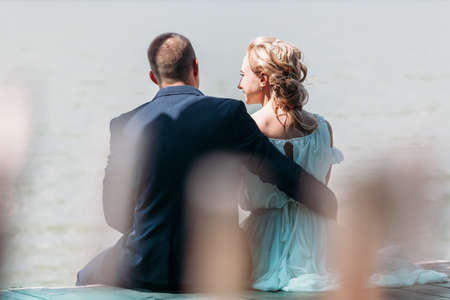 bride and groom sitting back at the lakeon a wooden pie.の写真素材