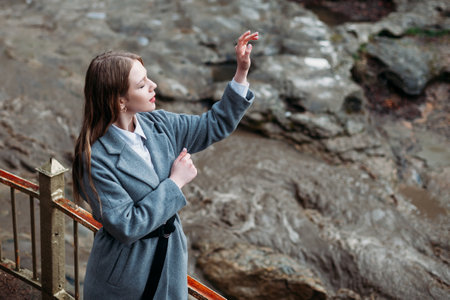 Portrait of a beautiful girl in a gray coat on a gray background of a mountain river. copy spaceの写真素材