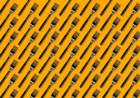 Many black plastic forks on yellow background, top view. Disposable table wear concept. Creative top view pattern.の写真素材
