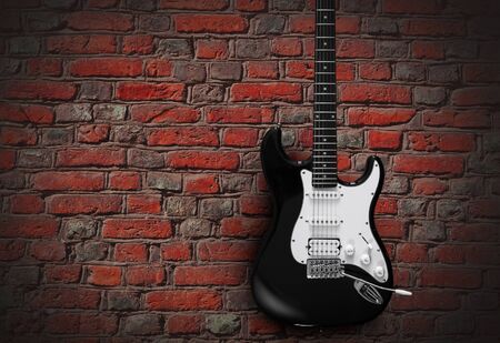 Black electric guitar on red brick wall background.の写真素材